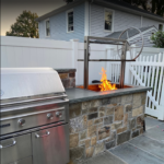 Live fire grill with grates raised over wood flames in a stone outdoor kitchen island